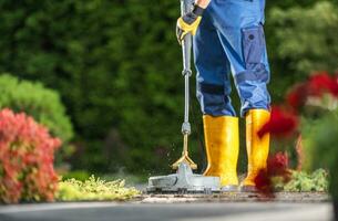 Caucasian Garden Keeper in His 40s Washing Concrete Bricks Driveway Using a Modern Pressure Washer photo