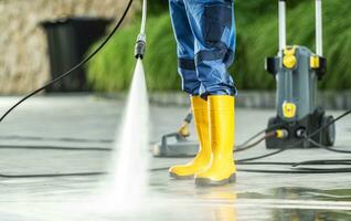 A Men Washing Residential Bricks Made Driveway and Paths Using Powerful Pressure Washer. Front Yard Maintenance Theme. photo