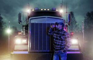 Professional Truck Driver Drinking Coffee in Front of His Semi Truck Tractor photo