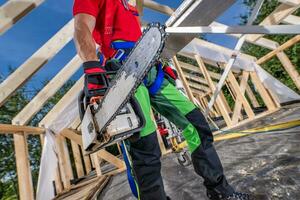 Worker with Chainsaw in His Hand Walking Along Wooden House Frame photo