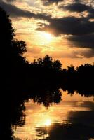 un puesta de sol terminado un lago con arboles y nubes foto