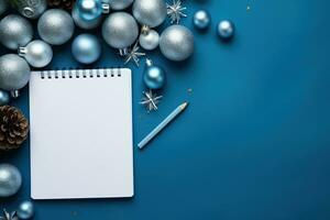 Christmas blue background with blank paper and blue metallic decorations on a table. Top view photo