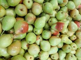 Large box with harvested ripe pears standing in green summer orchard,Green pears at the fresh market,texture background fruit,fresh packham pear to eat,green yellow Pear fruit with light reflections photo