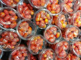 Fresh tomatoes packed in plastic glasses ready to eat,Fresh ripe tomatoes on counter at wholesale market,The packagging is red tomatos from organic fram.cherry tomatoes harvest in separate plastic box photo
