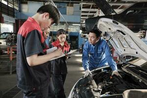 Asian male professional automotive engineer supervisor describes car engine maintenance and repair work with mechanic worker staffs team in fix service garage, specialist occupations in auto industry. photo