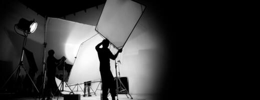 Silhouette of video production behind the scenes or B roll or making of TV commercial movie that film crew team lightman and cameraman working together with director in big studio with pro equipments photo