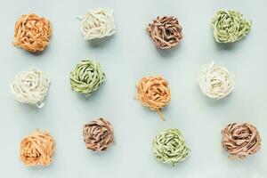 Raw traditional Italian tagliatelle pasta noodles nests of a different color spinach, potato, carrot, amaranth, light background. Natural vegetable food coloring concept. Close up, random pattern photo