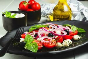 Caprese Italian or Mediterranean salad. Tomato mozzarella basil leaves black olives and olive oil on wooden table. photo