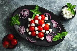 de cerca en un negro plato con Fresco caprese ensalada con albahaca, Cereza Tomates, mini queso Mozzarella pelotas, coronado con balsámico vinagre salsa en un gris de madera mesa, parte superior ver foto