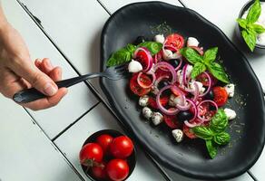 tomate y queso Mozzarella caprese ensalada y pesto salsa con aceitunas en blanco mesa servido con tenedor. comida italiano aperitivo foto