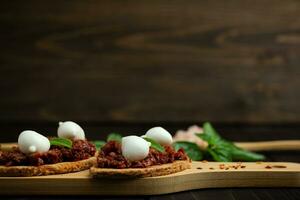 Bruschetta con seco Tomates, queso Mozzarella y albahaca en de madera antecedentes. Copiar espacio foto