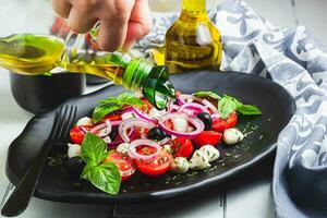 Caprese Salad with tomatoes mozzarella olives basil and olive oil on wooden table. photo
