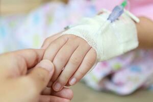 Mother holding child hand with saline IV solution in hospital photo