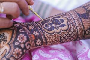 Young woman mehendi artist painting henna on the bride's hand photo