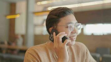 un joven hombre se sienta y negociaciones en el teléfono en un café tienda. video