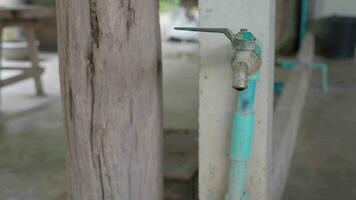 un antiguo agua grifo instalado en el lado de un cemento pilar en un rural casa goteado agua, causando residuos y pobreza, causando No refacción. video