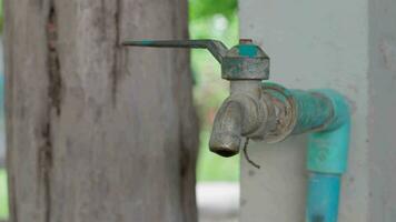 An old water faucet installed on the side of a cement pillar in a rural house dripped water, causing waste and poverty, causing no repairs. video