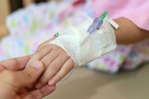 Mother holding child hand with saline IV solution in hospital photo