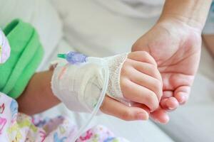 Mother holding child hand with saline IV solution in hospital photo