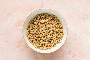 Delicious honey cheerios cereal in a bowl on pink background. Top view, flat lay, copy space. Breakfast concept photo