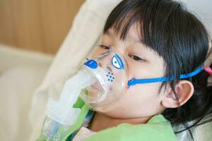 Sick little asian girl inhalation with nebulizer for respiratory treatment photo