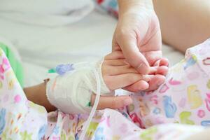 Mother holding child hand with saline IV solution in hospital photo