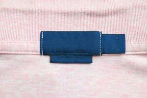 Blank blue laundry care clothes label on pink shirt fabric texture background photo