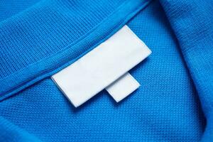 Blank white laundry care clothes label on blue shirt fabric texture background photo