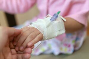 Mother holding child hand with saline IV solution in hospital photo