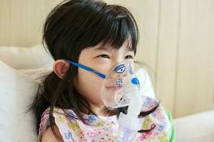 Sick little asian girl inhalation with nebulizer for respiratory treatment photo