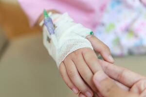 Mother holding child hand with saline IV solution in hospital photo