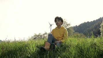 een jongen zittend in de gras met een wind turbine video