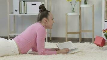 uma mulher deitado em a chão lendo uma livro e uma menina chegando com uma presente video