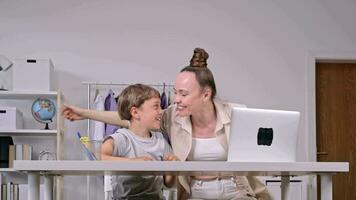 a woman and a child sitting at a table with a laptop video