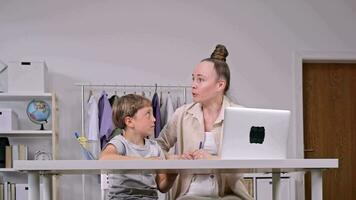 a woman and a child sitting at a desk with a laptop video