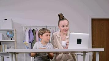 a woman and a child sitting at a table with a laptop video