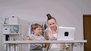 a woman and a child sitting at a desk with a laptop video