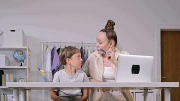 a woman and a child sitting at a desk with a laptop video