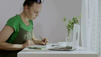 ein Frau im ein Schürze ist Arbeiten auf ihr Laptop video