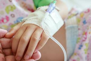 Mother holding child hand with saline IV solution in hospital photo