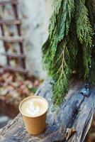 Takeaway coffee in paper cup on old rustic wooden bench in coffee shop with outdoor space with ecofriendly garden. Fall or winter garden with pine branch photo