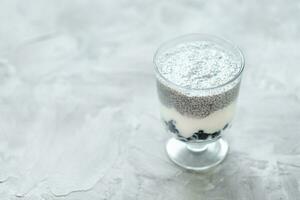 Chia seed pudding with almond milk, yogurt and blueberries dessert in a glass. Superfood and vegan food concept. Gray background. Copy space, selective focus photo