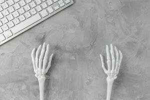 Halloween gray background with white skeleton hands and computer keyboard. Halloween holiday online shopping banner mockup. Top view, copy space photo