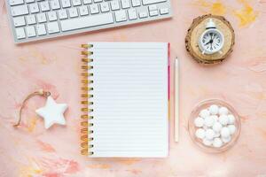 Notepad, pen, computer keyboard, clock, chocolate on woman desk workspace, pink background. Winter holidays preparation, goals, lifestyle concept. To Do List template. Flat lay, top view, mock up photo