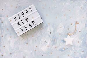 Words HAPPY NEW YEAR with silver stars confetti decoration on blue background. New Year preparation and celebration concept. Flat lay, top view, copy space photo