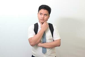 Indonesian senior high school student wearing white shirt uniform with gray tie and thinking about question with hand on chin. Isolated image on white background photo