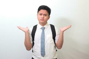 Confused senior high school student wearing white shirt uniform with gray tie spreading his hands sideways and holding two things, demonstrate products. Isolated image on white background photo