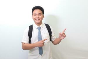 Indonesian senior high school student wearing white shirt uniform with gray tie showing product, pointing at something and smiling. Isolated image on white background photo