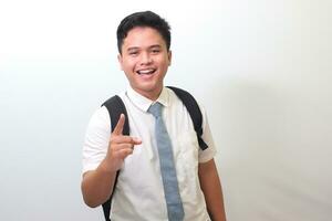 Indonesian senior high school student wearing white shirt uniform with gray tie showing product, pointing at something and smiling. Isolated image on white background photo