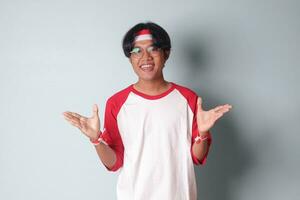 Portrait of attractive Asian man in t-shirt with red and white ribbon on head, pulling hands towards camera, inviting someone to come inside, welcoming gesture. Isolated image on gray background photo